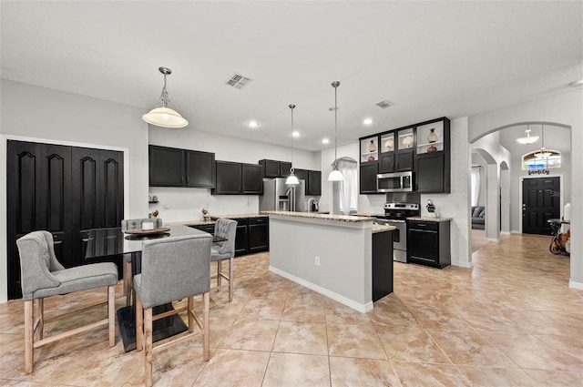 kitchen featuring arched walkways, pendant lighting, stainless steel appliances, glass insert cabinets, and a kitchen island