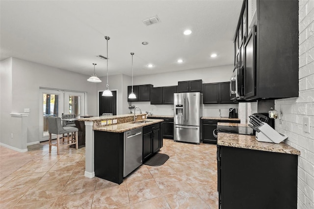 kitchen with hanging light fixtures, light stone counters, stainless steel appliances, a center island with sink, and french doors