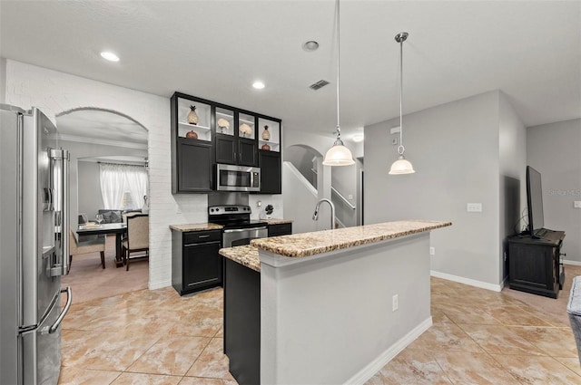 kitchen with appliances with stainless steel finishes, decorative light fixtures, an island with sink, light stone counters, and crown molding