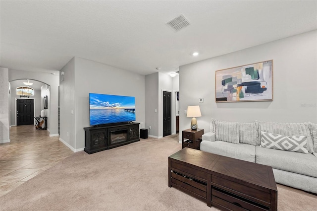 living area featuring arched walkways, light carpet, visible vents, and baseboards