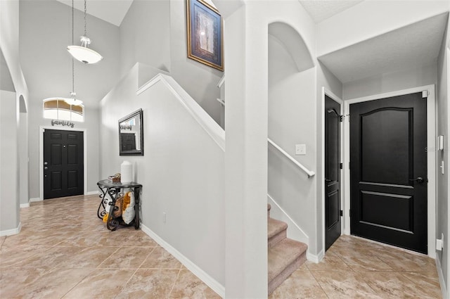 entryway with light tile patterned floors, stairs, baseboards, and high vaulted ceiling