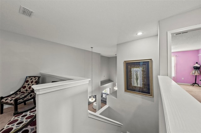 hallway with an upstairs landing, light carpet, visible vents, and a textured ceiling