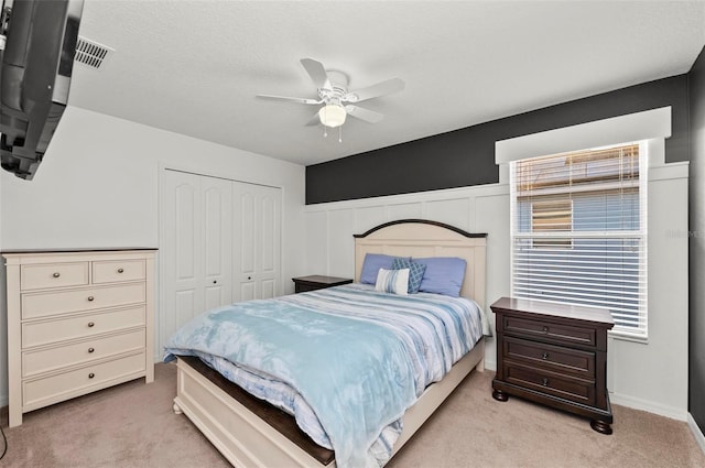 bedroom featuring a closet, light colored carpet, ceiling fan, and a wainscoted wall