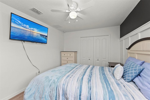 carpeted bedroom with a textured ceiling, visible vents, baseboards, a ceiling fan, and a closet