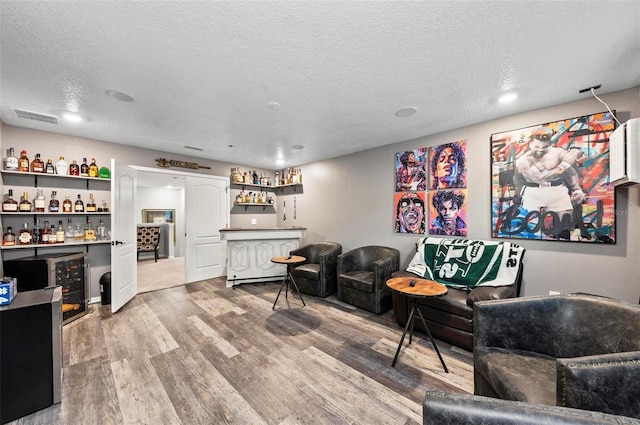 living room featuring hardwood / wood-style flooring, bar, a textured ceiling, and wine cooler