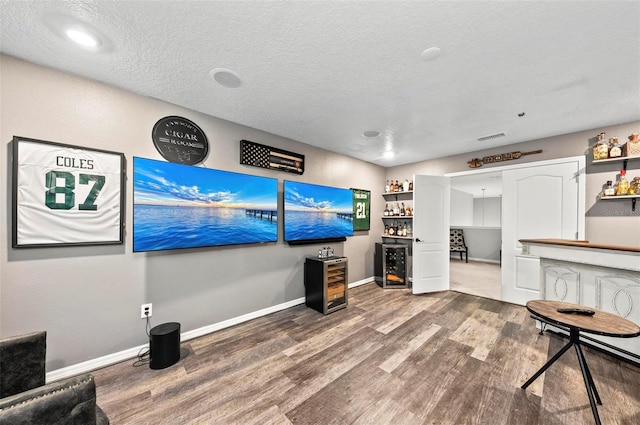 living room with wood-type flooring, bar, beverage cooler, and a textured ceiling