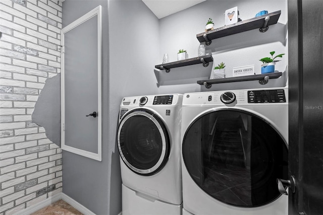 clothes washing area featuring baseboards, laundry area, brick wall, and washer and dryer