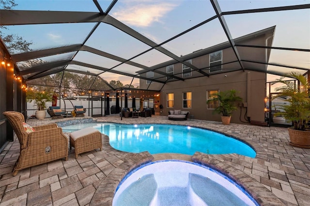 pool at dusk featuring a patio area, an outdoor hangout area, glass enclosure, and an in ground hot tub