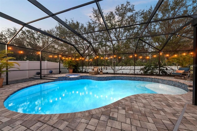 pool at dusk featuring an in ground hot tub, glass enclosure, and a patio