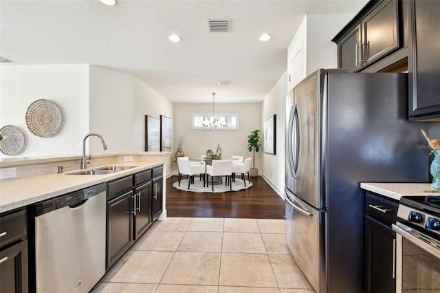 kitchen featuring light tile patterned flooring, appliances with stainless steel finishes, decorative light fixtures, sink, and a textured ceiling