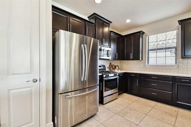 kitchen with appliances with stainless steel finishes, dark brown cabinets, light tile patterned floors, and tasteful backsplash