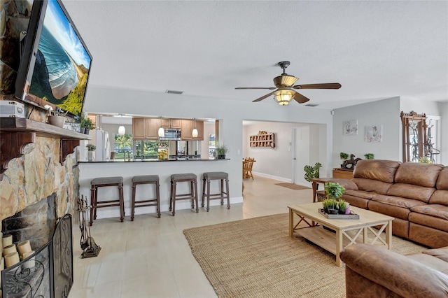 living room featuring ceiling fan, a stone fireplace, and a textured ceiling