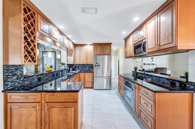 kitchen with light tile patterned floors, stainless steel appliances, kitchen peninsula, and dark stone counters