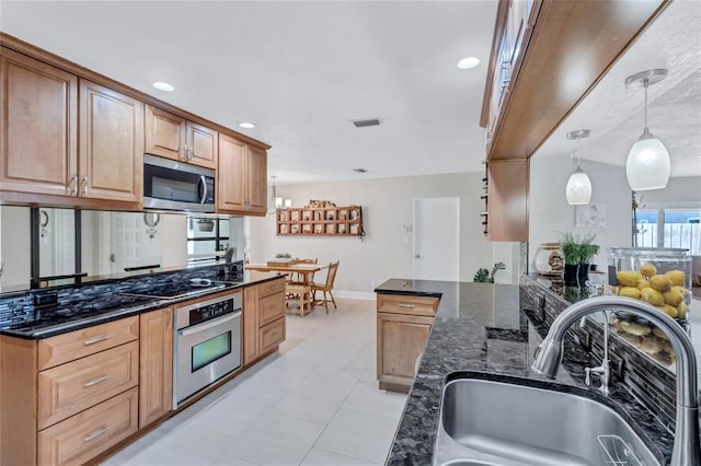 kitchen featuring sink, light tile patterned floors, dark stone countertops, appliances with stainless steel finishes, and pendant lighting