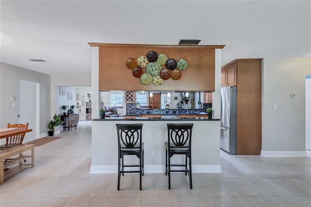 kitchen featuring decorative backsplash, a kitchen breakfast bar, stainless steel refrigerator, and kitchen peninsula