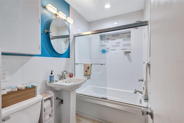 bathroom with enclosed tub / shower combo, toilet, and tile walls