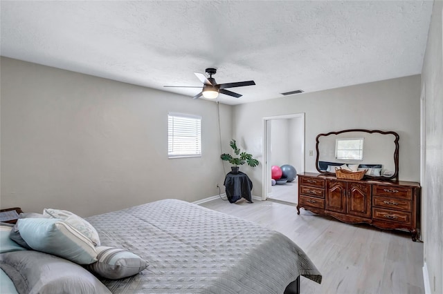 bedroom with a textured ceiling, light hardwood / wood-style flooring, and ceiling fan