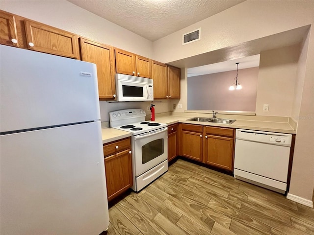 kitchen featuring pendant lighting, sink, white appliances, light hardwood / wood-style flooring, and a textured ceiling