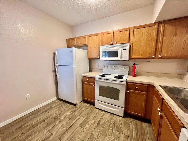 kitchen with white appliances, sink, light hardwood / wood-style floors, and a textured ceiling