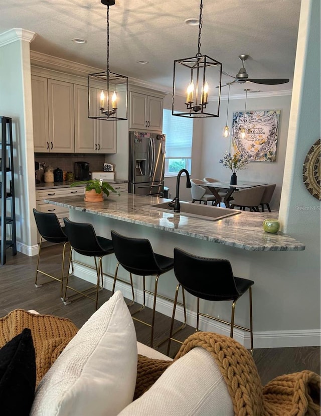 kitchen with sink, pendant lighting, light stone counters, and stainless steel fridge with ice dispenser