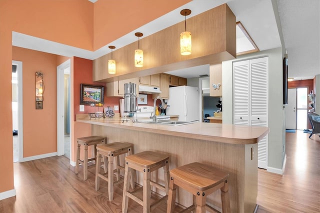 kitchen featuring light hardwood / wood-style flooring, a kitchen breakfast bar, kitchen peninsula, and white fridge