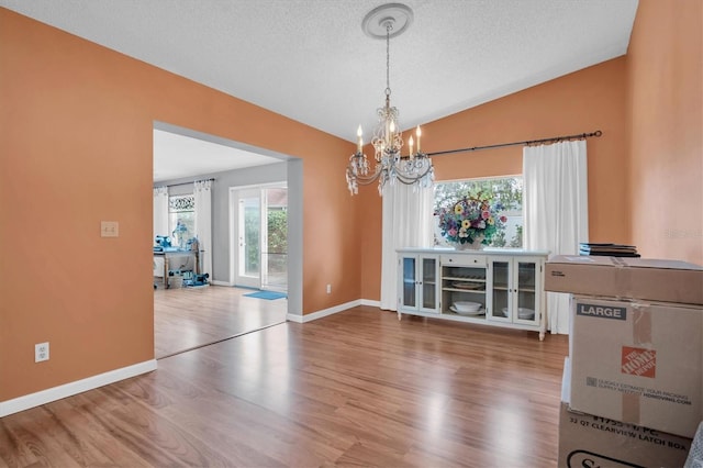 unfurnished dining area with hardwood / wood-style flooring, lofted ceiling, a textured ceiling, and a notable chandelier