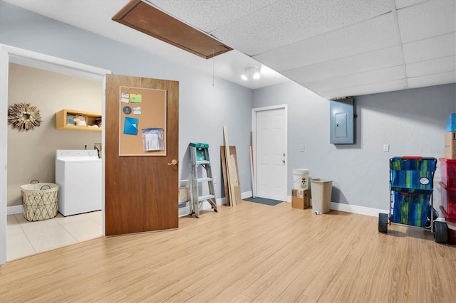 interior space featuring washer / dryer, a drop ceiling, electric panel, and light hardwood / wood-style floors