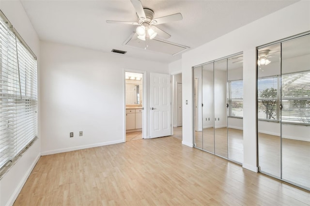 unfurnished bedroom featuring ceiling fan, two closets, light hardwood / wood-style floors, and ensuite bath