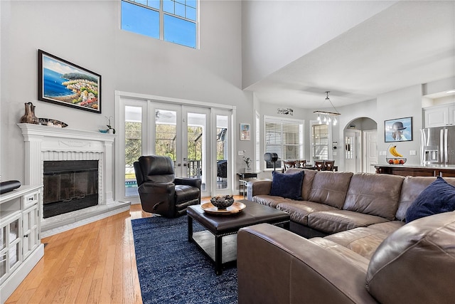 living room with a high ceiling, a brick fireplace, light hardwood / wood-style floors, and french doors