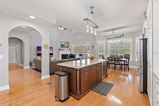 kitchen with stainless steel refrigerator, dark brown cabinetry, light hardwood / wood-style floors, a kitchen island, and decorative light fixtures