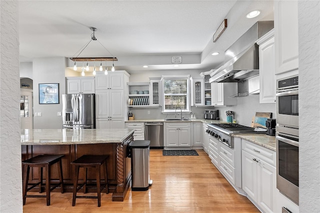 kitchen with sink, appliances with stainless steel finishes, white cabinetry, light hardwood / wood-style floors, and decorative light fixtures