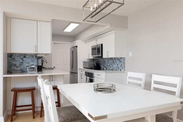 kitchen with sink, a breakfast bar, white cabinetry, hanging light fixtures, and stainless steel appliances