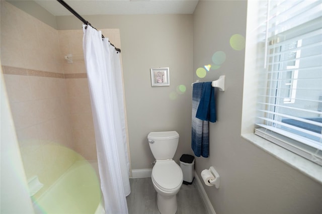 bathroom featuring a healthy amount of sunlight, shower / bathtub combination with curtain, and toilet