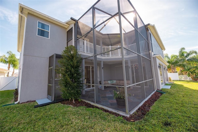 back of house featuring a balcony, a yard, glass enclosure, and a patio