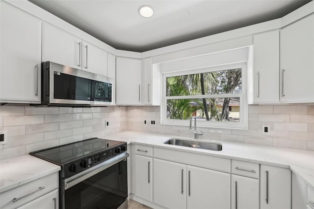 kitchen featuring electric range oven, white cabinetry, sink, backsplash, and light stone counters