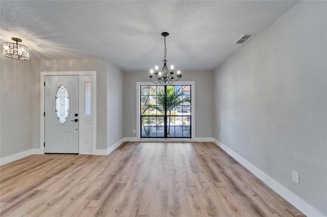 foyer entrance featuring an inviting chandelier, light hardwood / wood-style floors, and a textured ceiling