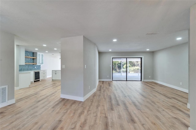 unfurnished living room featuring indoor bar, beverage cooler, and light hardwood / wood-style flooring