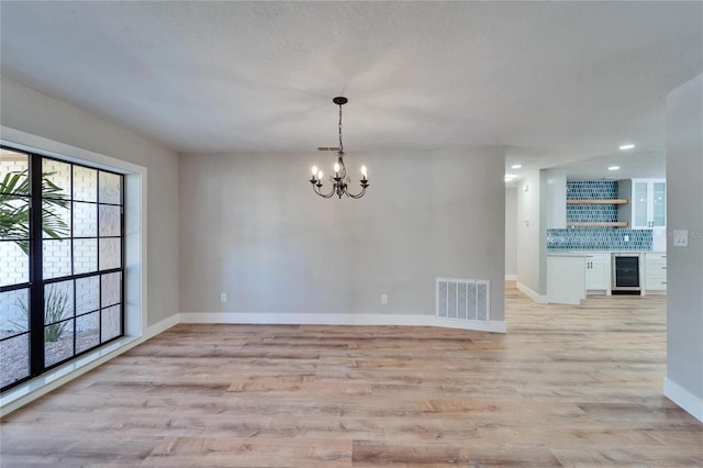 unfurnished room featuring an inviting chandelier, bar area, beverage cooler, and light wood-type flooring