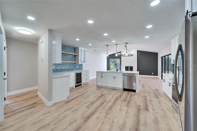 kitchen featuring appliances with stainless steel finishes, white cabinets, pendant lighting, beverage cooler, and backsplash