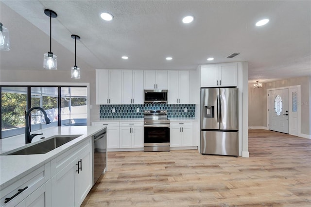 kitchen featuring sink, hanging light fixtures, light wood-type flooring, appliances with stainless steel finishes, and white cabinets