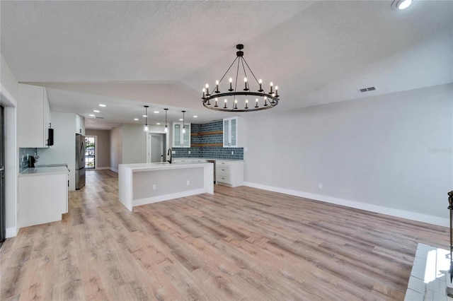 kitchen with a kitchen island with sink, hanging light fixtures, tasteful backsplash, white cabinets, and vaulted ceiling