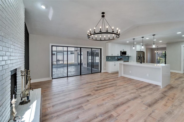 kitchen with vaulted ceiling, white cabinetry, hanging light fixtures, an inviting chandelier, and a spacious island