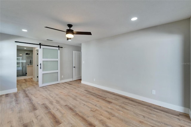 interior space with a barn door, ceiling fan, and light wood-type flooring