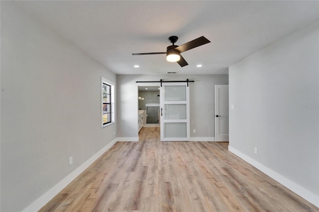 unfurnished bedroom with light hardwood / wood-style floors, a barn door, and ceiling fan