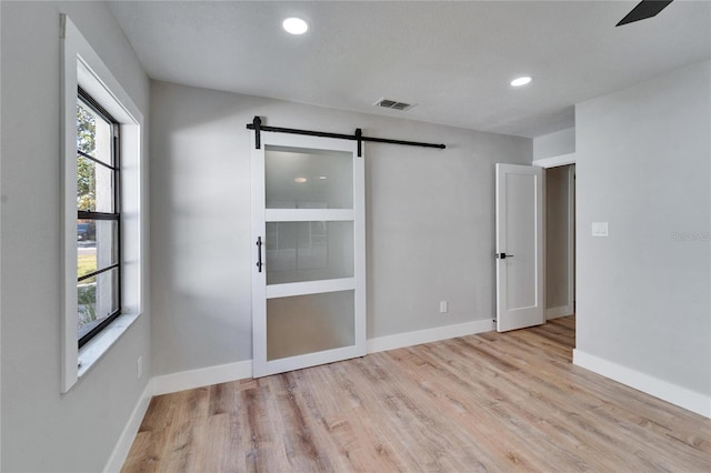 unfurnished room with a barn door and light wood-type flooring