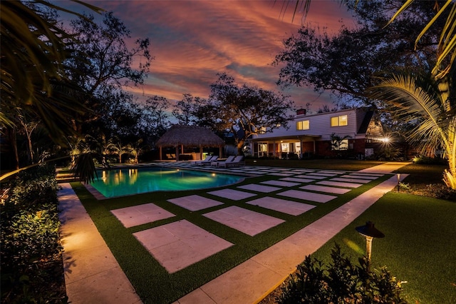 pool at dusk with a gazebo, a lawn, and a patio area