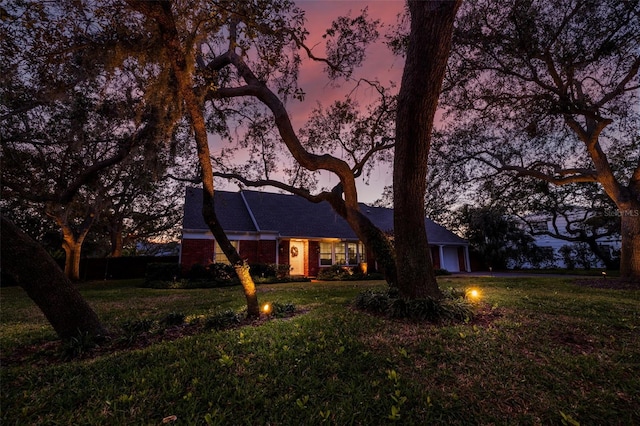 back house at dusk featuring a garage and a yard