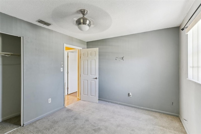 unfurnished bedroom with ceiling fan, a closet, light carpet, and a textured ceiling