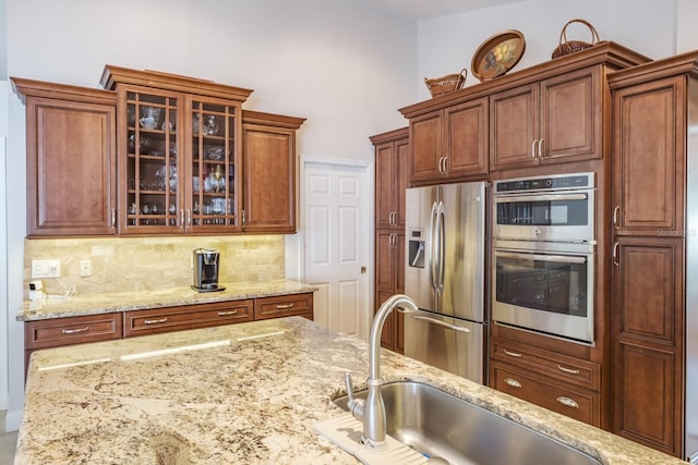 kitchen with tasteful backsplash, sink, light stone countertops, and appliances with stainless steel finishes