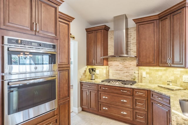 kitchen with stainless steel appliances, wall chimney range hood, backsplash, and light stone counters